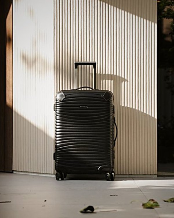 A black hard-shell suitcase standing against a fluted wall in raking afternoon light.
